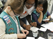 Scouts Sloane (left) and Katie (far right) listen to student volunteer Jasmin Wright explain the M&M chromatography experiment. Students separate the food dye mixtures used to color the candy coatings. The dyes' properties determine how fast they creep up the filter paper when immersed in salt water, resulting in separation.
